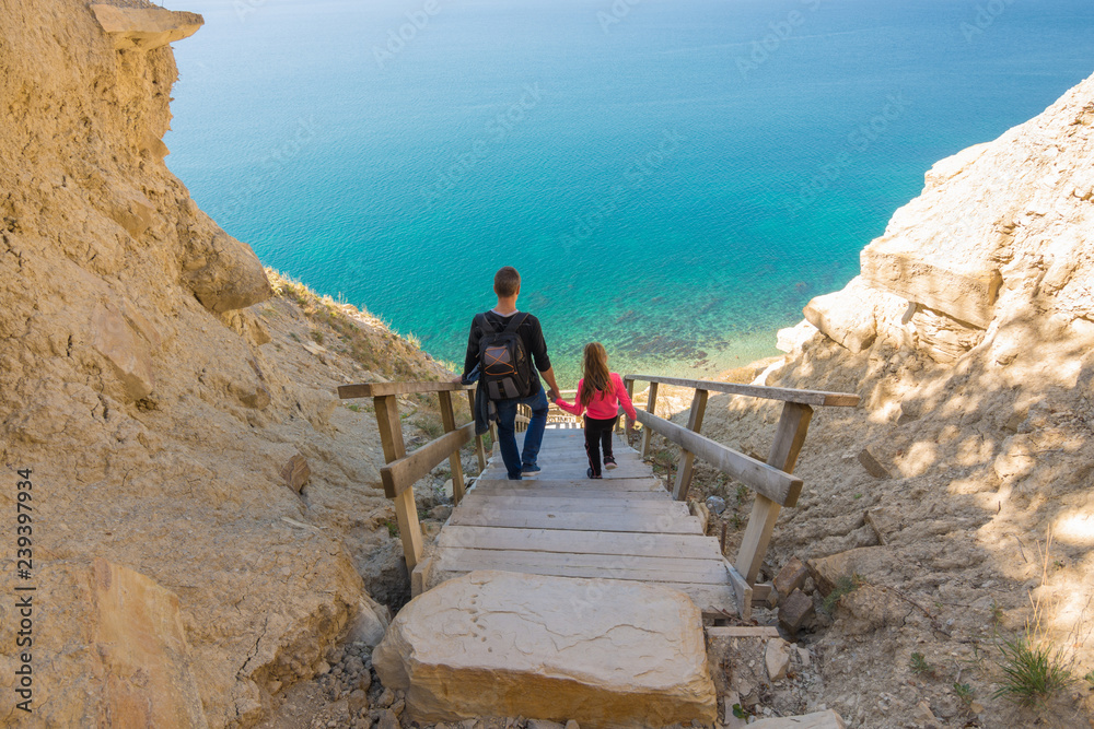 Dad and daughter go down the steep mountain stairs to the sea