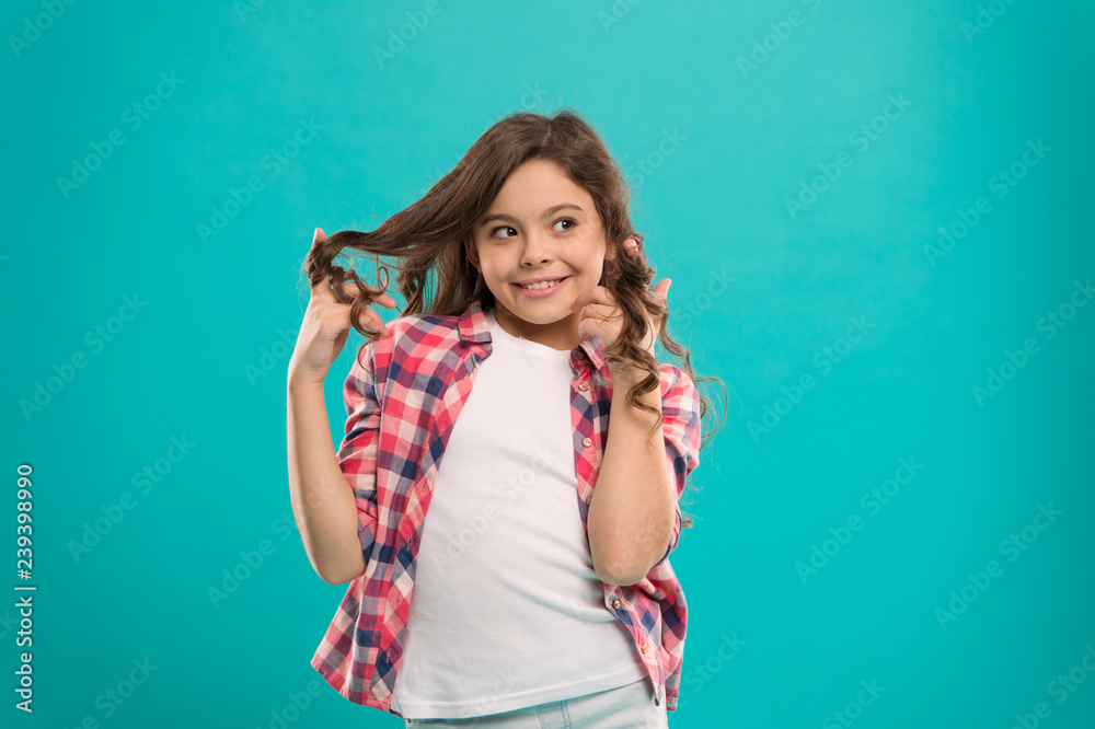 Playful curls. Beauty tips for tidy hair. Kid girl long healthy shiny hair wear casual clothes. Little girl with long hair. Kid happy cute face with adorable curly hair stand over blue background Playful curls. Beauty tips for tidy hair. Kid girl long healthy shiny hair wear casual clothes. Little girl with long hair. Kid happy cute face with adorable curly hair stand over blue background