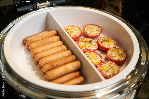 Tomato gratin and beef sausages in pan on electric kitchen stove
