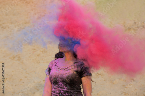 Pretty brunette woman with long wavy hair having fun with pink and blue dry Holi powder at the desert
