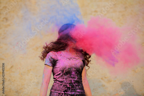 Young brunette girl with long wavy hair having fun with pink and blue dry Holi powder at the desert