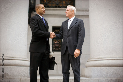 Two suited businessmen shaking hands outside a building in the city. photo