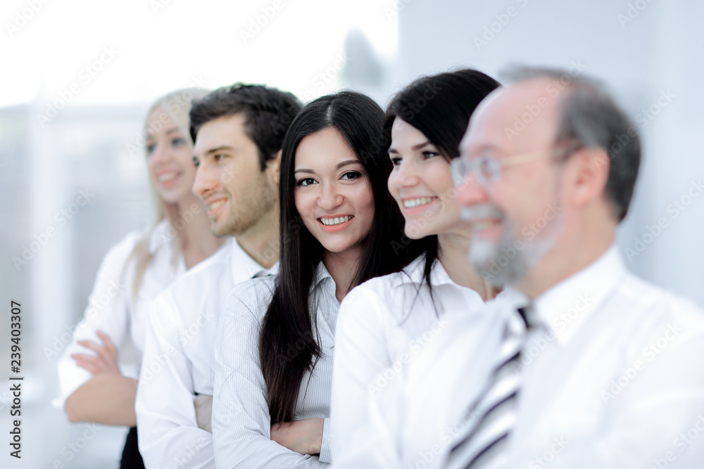 Close-up of a business woman in selective focus looking at a camera with her colleagues in formal wear standing behind her in a row in blurry Close-up of a business woman in selective focus looking at a camera with her colleagues in formal wear standing behind her in a row in blurry