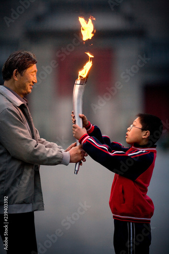 Mature adult man holding a lit torch with his grandson.