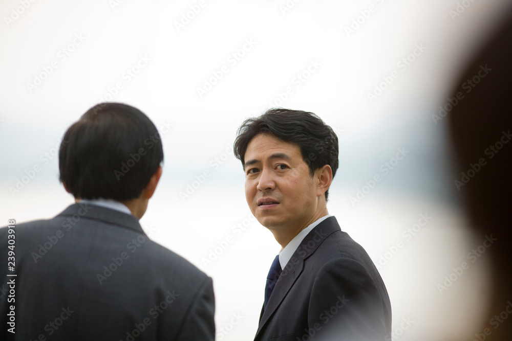 Portrait of a mid-adult businessman standing outdoors with a colleague. Portrait of a mid-adult businessman standing outdoors with a colleague.