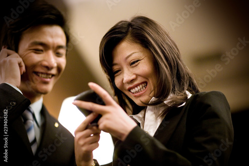 Mid-adult business woman looking at a cellphone with a male colleague on a cellphone in an office.