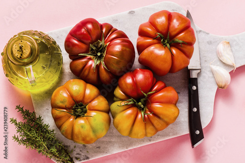 brandywine tomato on a cutting board. cooking summer salad with fresh olive oil, thyme. on a rose background photo