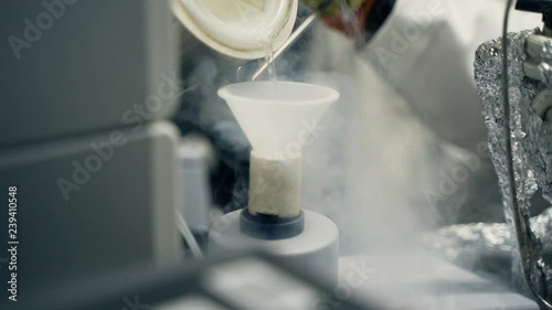 Slow motion pouring liquid nitrogen through a funnel into container in laboratory photo