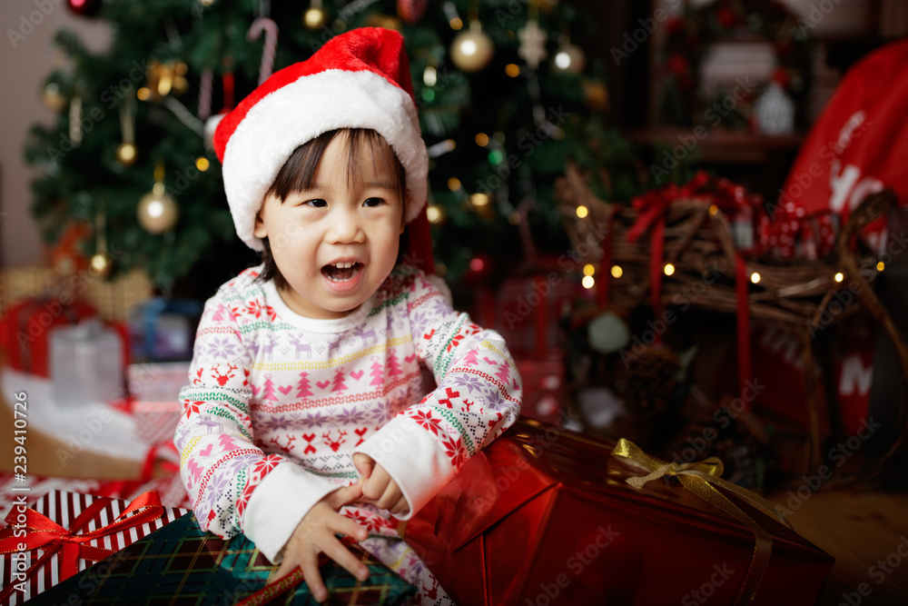 toddler baby girl wearing santa claus costume open gift box  in front of christmas tree