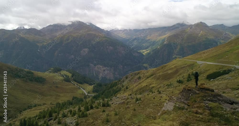 Woman standing on a mountain ridge, C4k aerial, tracking, drone shot, of a girl posing on a ridge, on Grossglockner mountain pass, on a cloudy, summer day, in the alps of Austria Woman standing on a mountain ridge, C4k aerial, tracking, drone shot, of a girl posing on a ridge, on Grossglockner mountain pass, on a cloudy, summer day, in the alps of Austria