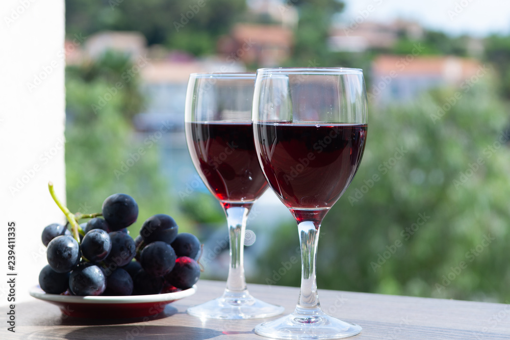 Two wine glasses with red wine served with red grape on outdoor terrace