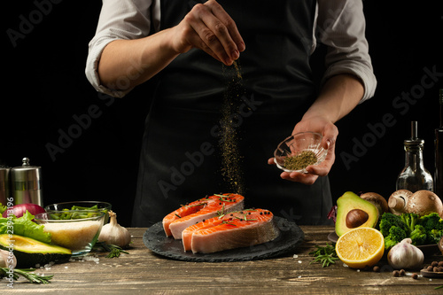 Fototapeta Naklejka Na Ścianę i Meble -  The chef prepares fresh salmon fish, fresh salmon, sprinkles with spices and Provencal herbs with ingredients.Frost in the air. cooking fish food.Cooking vegan cuisine, restaurants,hotel business