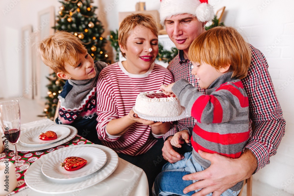 Happy family with children eating cake at the Christmas table. Baby smeared  mom's nose with cake having fun Stock Photo | Adobe Stock