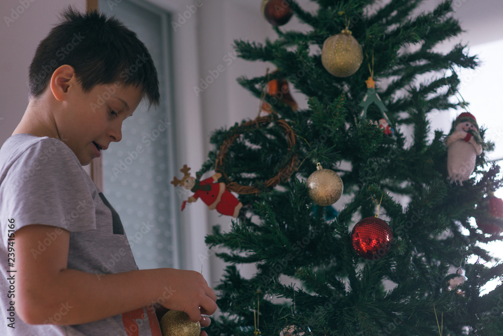 Happy boy is decorating the Christmas tree with red and yellow decoration.