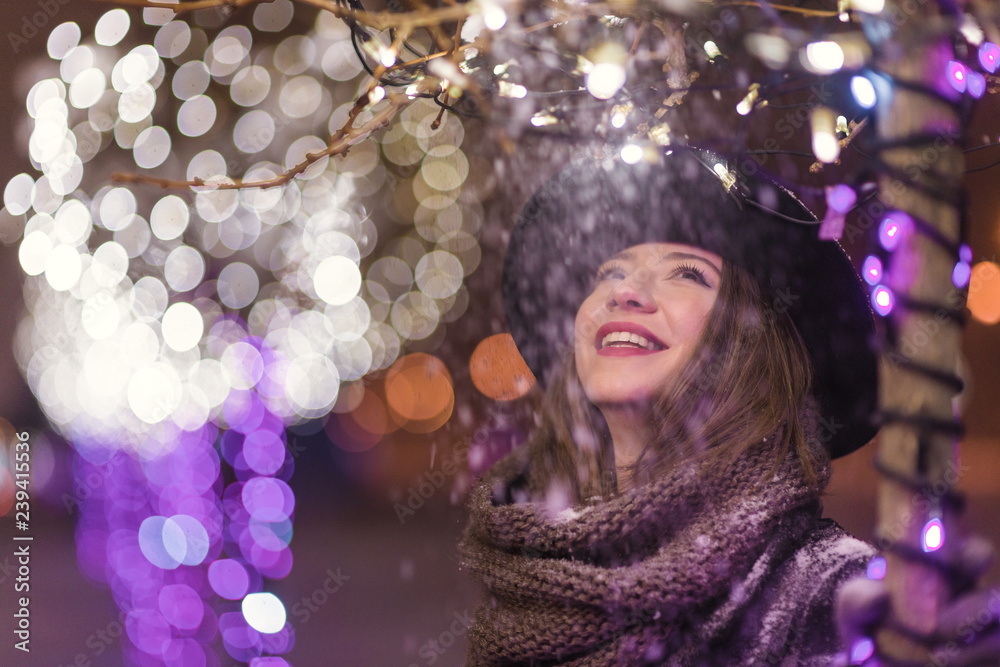 Young girl standing in front of christmas tree lights at night with snowflakes falling, snowing Young girl standing in front of christmas tree lights at night with snowflakes falling, snowing