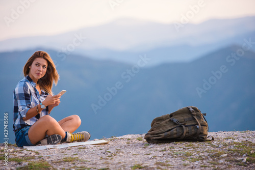 Young lady checking her phone and marveling the view from the top of the world at sunset. Success, winner, zen, tranquility.