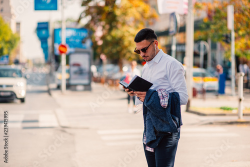 Handsome businessman is in the city, talking and walking on the street, holding notebook in his hands.