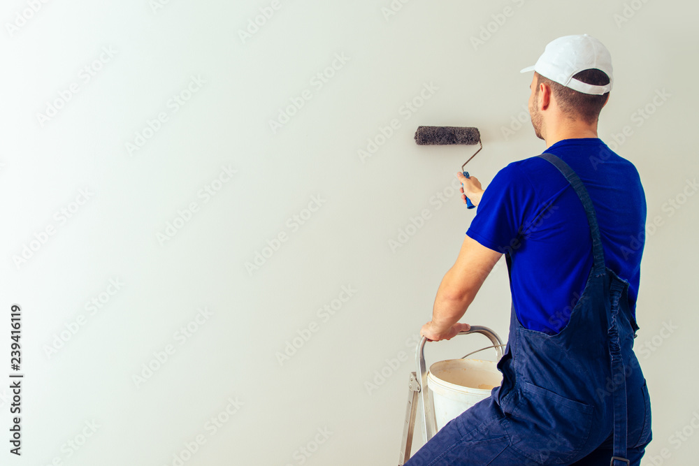 Young decorator on ladder painting wall into the white Young decorator on ladder painting wall into the white