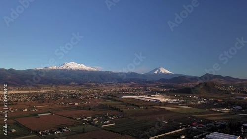 Ascending aerial shot above countryside views chalco, Mexico. Background view of two volcanoes Iztaccihuatl and Popocat√©petl lit by sunset on snowy tops. photo