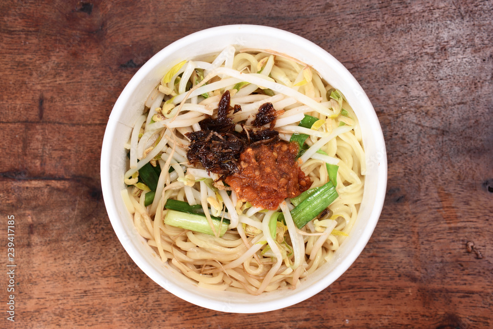 Noodles with vegetables and chili sauce in take-out  food container on wooden table  