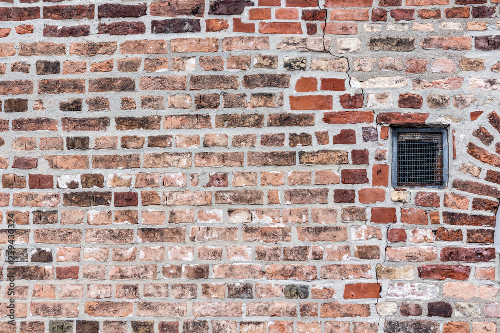 Fototapeta premium Brick old textured wall wall with a small window with a lattice. texture of brickwork from multicolored terracotta red bricks