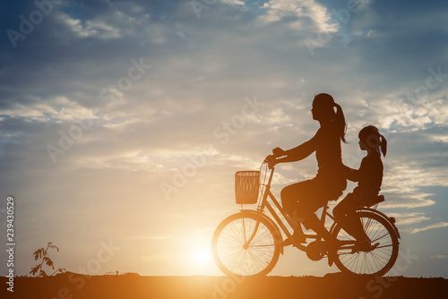 Silhouette of mother with her daughter and bicycle