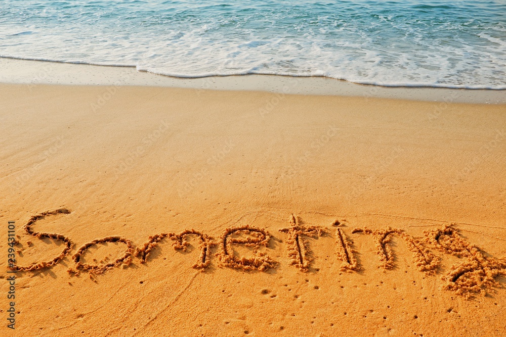 Fototapeta premium The word someting handwriting on sand beach with blue waves background.