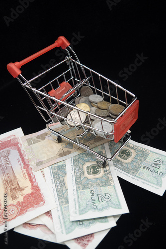 Small shopping cart with coin on bank notes with black background. background concept for shopping and e-commerce