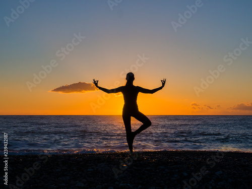Silhouette of young woman doing exercises on the sea beach during sunset. Yoga, fitness and a healthy lifestyle
