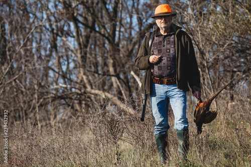 Elderly hunter with wild bird in orange hat