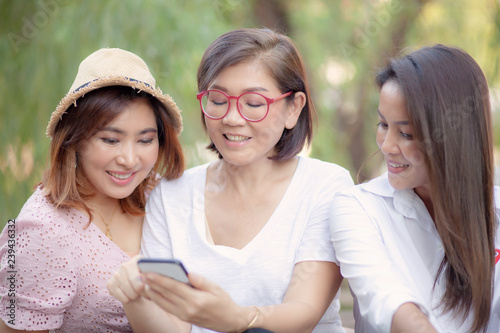 three asian woman looking on mobile phone screen with toothy smiling face