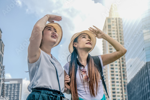 two Asian female tourist traveler having city tour in hot day and having hands cover faces from sun light while looking to landmark © Mongkolchon