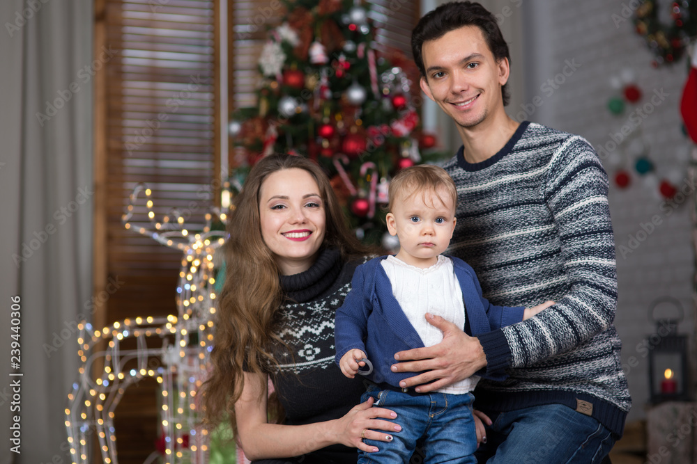 family sits with the baby sitting near the Christmas tree,