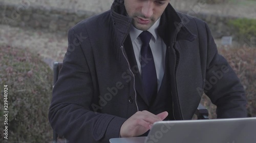 Pan down on businessman working on laptop and arranging his coat photo