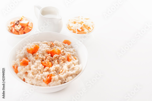 Oatmeal with pumpkin and nuts in a plate, vegetable salad and a jug with milk on a white background. Close-up. Copy space