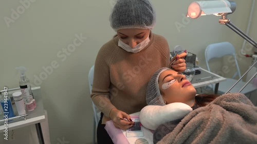 Very concentrated female eyelash master is making eyelash extension to female customer. Close-up portrait. photo