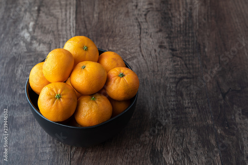 Black bowl of satsuma oranges on a rustic wood table