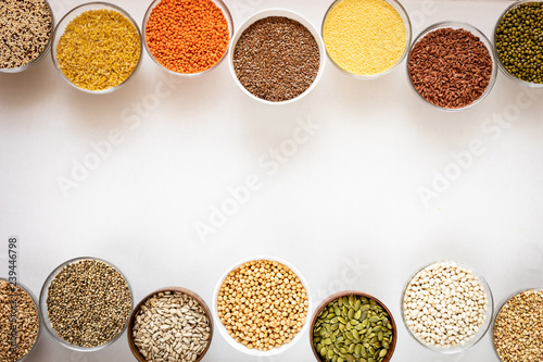 Top view to glass bowls with cereals, beans and seeds on white background with copy space in middle.