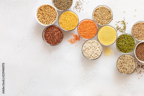 Diagonal flat lay glass bowls with cereals, beans and seeds on white background with copy space.