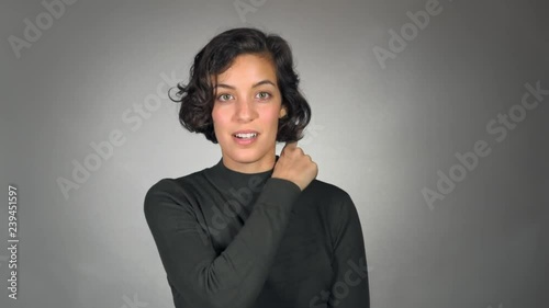 Isolated against a grey studio backdrop, a young woman looks at the camera and slides her finger humorously across her neck, suggesting violence or conflict