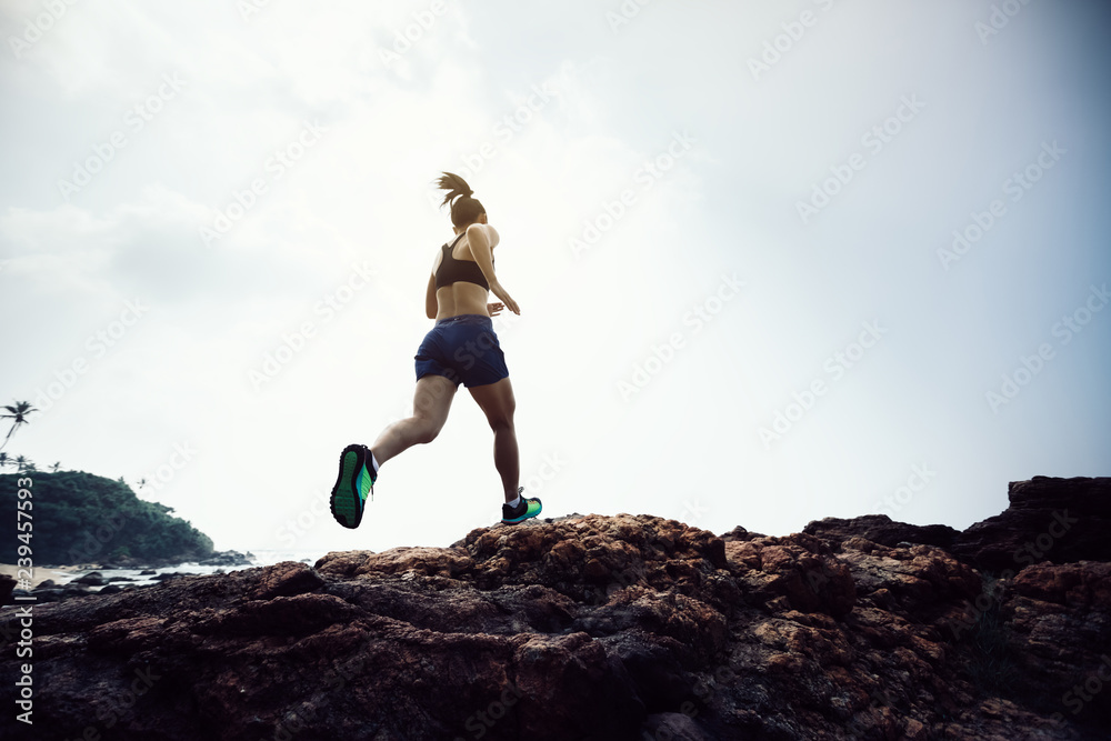 Woman trail runner running to rocky mountain top on seaside Woman trail runner running to rocky mountain top on seaside