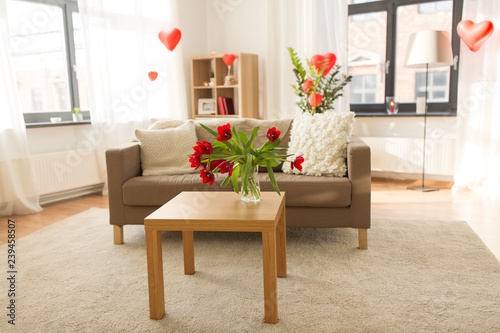 valentines day, holidays and interior concept - red flowers on table in living room or home decorated with heart shaped balloons © Syda Productions
