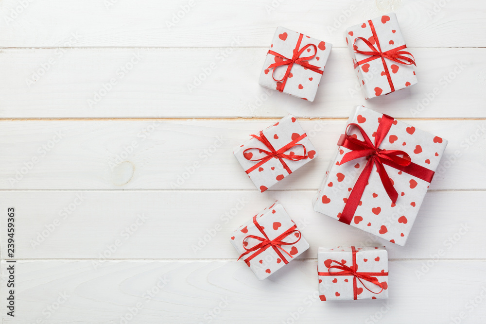 Valentine or other holiday handmade present in paper with red hearts and gifts box in holiday wrapper. Present box gift on white wooden table top view with copy space, empty space for design