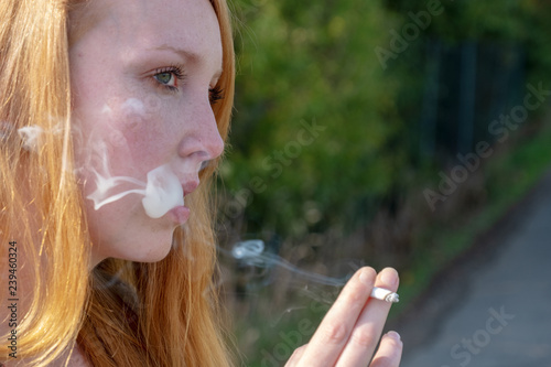 Portrait einer jungen sexy rothaarigen, rotblonden Frau, die genüßlich im Freien Ringe des Rauches einer Zigarette ausbläst, mit Raum Platz für Ihren Text, Textfreirau photo