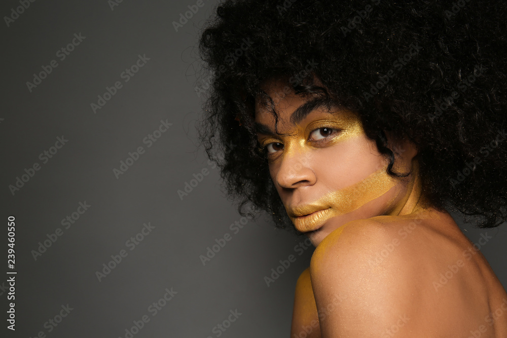 African-American woman with golden paint on her body against dark background African-American woman with golden paint on her body against dark background