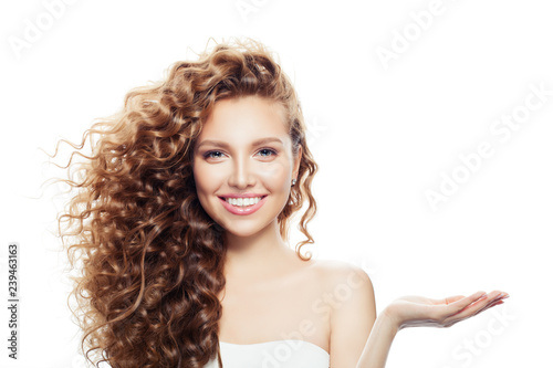 Cheerful woman with long curly hair, clear skin and empty open hand isolated on white background