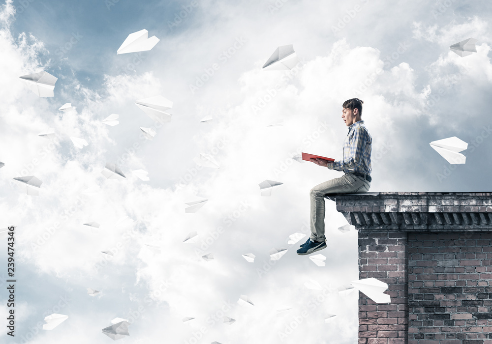 Handsome student guy on roof edge reading book and paper planes Handsome student guy on roof edge reading book and paper planes