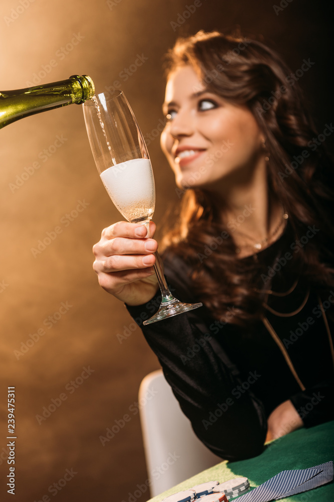 selective focus of waiter pouring champagne in glass for attractive smiling girl at poker table in casino selective focus of waiter pouring champagne in glass for attractive smiling girl at poker table in casino