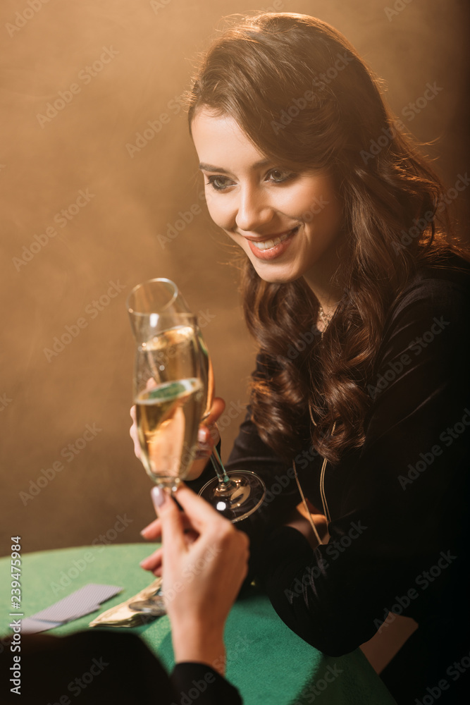 happy attractive girls clinking with glasses of champagne at poker table in casino
