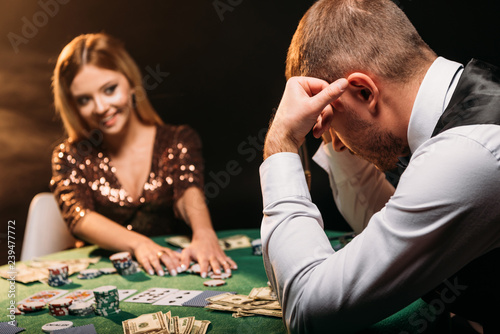 Canvas Print smiling attractive girl taking poker chips and looking at sad croupier at casino